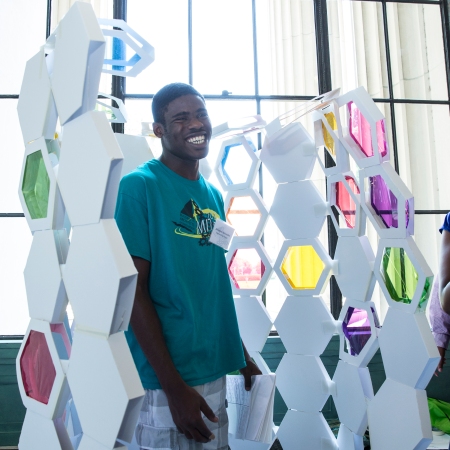 Engineering Design program student Jeremiah Akinsulire of Jamaica, NY steps into “The Busy Bee,” a model phone booth made by Architecture program students Jennah Jones of Chapel Hill, NC, Carlos Romero of Boston, MA, Emanuel Perez of Chicago, IL and Diondra Dilworth of Las Vegas, NV.
